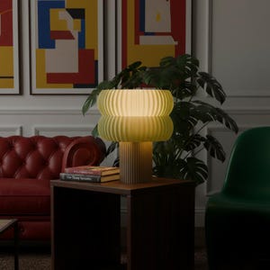May include: A table lamp with a cylindrical base and a double-tiered, rounded shade, both featuring a vertical ribbed texture. The lamp emits a soft, warm glow, illuminating the surrounding area while resting on a dark wooden surface.