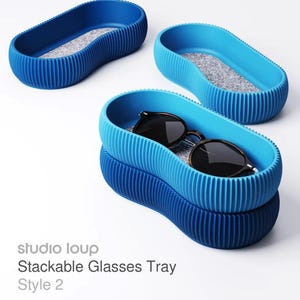 May include: Stackable glasses tray in shades of blue, with a textured, ribbed design. The tray has a gray interior and holds a pair of sunglasses. The text "studio loup" and "Stackable Glasses Tray Style 2" are visible.
