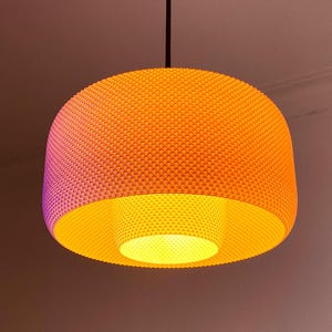 May include: Orange and yellow pendant light fixture. The light has a textured, spherical shade with a cylindrical inner shade. The light is suspended from a black cord. The light fixture is a modern design.