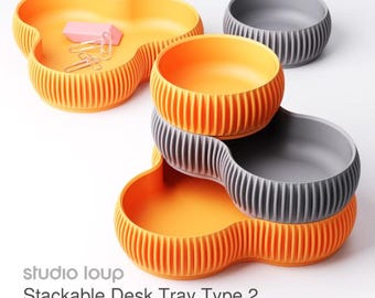 May include: Orange and grey stackable desk trays with a ribbed design. The trays are in a clover-like shape. The text "studio loup Stackable Desk Tray Type 2 Style 2" is visible.