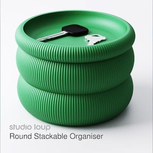 May include: A green, stackable organizer with a ribbed texture. The organizer has a round shape and holds two keys. The text "studio loup" and "Round Stackable Organiser" are visible on the bottom.