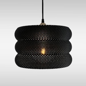 May include: Black pendant light fixture with a unique, textured design. The light has a cylindrical shape with three stacked sections. The fixture hangs from a black cord and emits a warm, inviting glow.