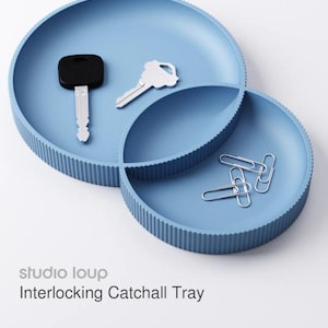 May include: A light blue interlocking catchall tray with a ribbed edge. The tray holds a black car key, a silver key, and three silver paper clips. The text "studio loup" and "Interlocking Catchall Tray" are visible.