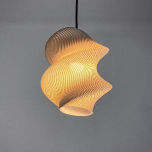 May include: A modern, beige-colored pendant light fixture with a unique, swirling design. The light has a textured surface and emits a warm, inviting glow. The fixture is suspended from a black cord, creating a stylish and contemporary look.
