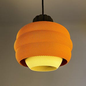 May include: A modern pendant light fixture with a textured orange shade and a yellow interior. The light hangs from a black cord and has a dark brown decorative cap. The shade has a unique, dimpled pattern.