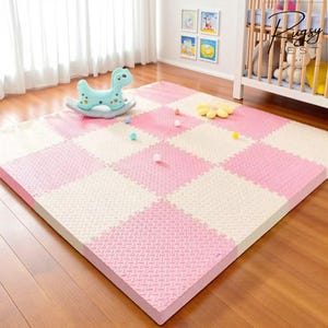 Puede incluir: Una gran alfombra de juego de espuma entrelazada con un patrón de cuadros rosas y crema. Un caballito balancín azul y pequeños juguetes están sobre la alfombra. La alfombra está diseñada para el área de juegos de un bebé o niño pequeño.