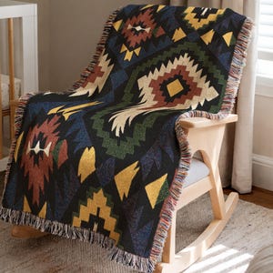 May include: A woven throw blanket with a geometric pattern in shades of black, brown, yellow, blue, and green is draped over a wooden rocking chair. The blanket has a fringed edge and a Southwestern design.
