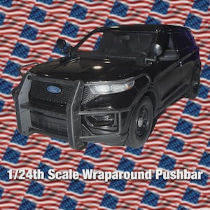 Op de afbeelding: Zwart Ford SUV-model met een wraparound pushbar. Het model is 1/24 schaal. De achtergrond heeft een patroon van Amerikaanse vlaggen.