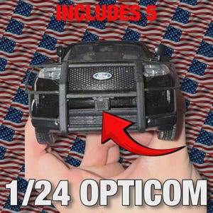 Op de afbeelding: Een zwart Ford politieautomodel met een push bar, vastgehouden in een hand. Het model is schaal 1/24 en heeft de tekst "OPTICOM". De achtergrond heeft een herhaald patroon van Amerikaanse vlaggen, met de tekst "INCLUDES 5".