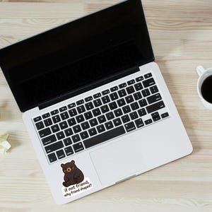 May include: Laptop with a black screen and keyboard, a sticker of a brown bear with the text "if not friend, why friend shaped?", a cup of coffee, pencils, and crumpled paper on a light wood surface.