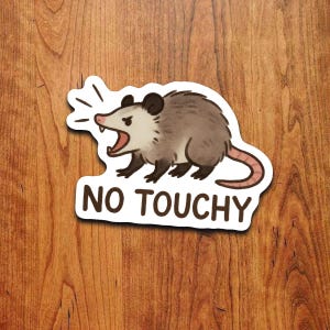 May include: A sticker depicting a cartoon opossum with an open mouth and the words "NO TOUCHY" in white. The opossum is grey with a pink nose and tail, and black ears and feet. The sticker is on a wooden surface.