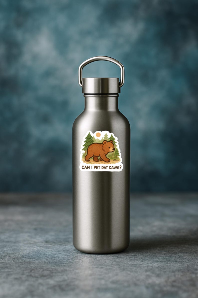 May include: A silver water bottle with a sticker depicting a brown bear in a forest setting. The sticker has the text "CAN I PET DAT DAWG?" in a fun font. The background is a blurred blue.