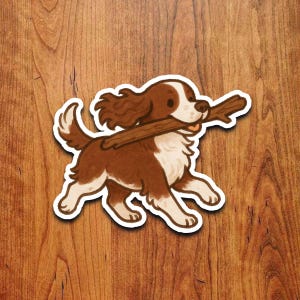 Op de afbeelding: Een sticker met een cartoonhond, bruin en wit, die rent met een bruine stok in zijn bek. De hond heeft flaporen en een pluizige staart. De sticker heeft een witte rand.