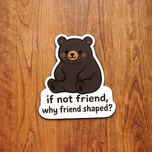 May include: A sticker featuring a cartoon black bear with a friendly expression and rosy cheeks. The bear sits on a white cloud-shaped background with the text "if not friend, why friend shaped?"