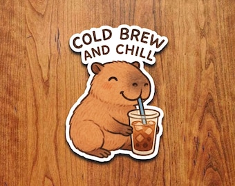 May include: A sticker featuring a cartoon capybara enjoying a cold brew coffee. The capybara is brown with a smiling face and is holding a clear cup with ice cubes and a blue straw. The text "COLD BREW AND CHILL" is above the capybara.