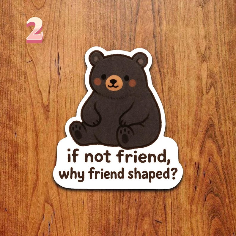 Puede incluir: Una pegatina con un oso negro de dibujos animados con una expresi&oacute;n amigable y mejillas rosadas. El oso est&aacute; sentado encima del texto "if not friend, why friend shaped?" El n&uacute;mero "2" est&aacute; en la esquina superior izquierda.