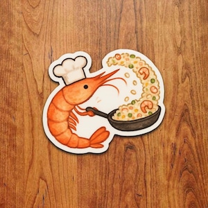 May include: A cartoon-style sticker of an orange shrimp wearing a chef's hat, holding a pan of rice and vegetables. The illustration has a white border. The shrimp is cooking a meal, with the rice spilling out.