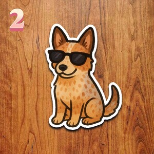 May include: A sticker featuring a cartoon dog wearing black sunglasses. The dog has brown and white fur with a smiling expression. The number "2" is in the upper left corner of the image.