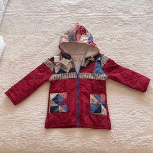 May include: A quilted jacket with a patchwork hood and pockets. The jacket is primarily red with a blue zipper and features various patterned fabric squares. The hood and pockets have a mix of floral and geometric designs.