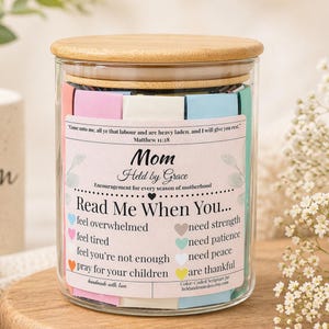 May include: A glass jar with a wooden lid, containing colourful notes. The jar's label says "Mom Held by Grace" and "Read Me When You..." with prompts. A sentimental gift for a mother.