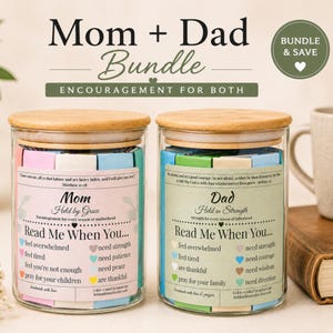 Peut inclure: Deux bocaux en verre transparent avec des couvercles en bambou, remplis de bandes de papier colorées. Le bocal de gauche porte une étiquette rose intitulée Mom Held by Grace, et celui de droite une étiquette verte intitulée Dad Held in Strength. Les deux bocaux présentent des textes incitant à la lecture en cas de besoin de soutien.