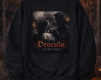 Puede incluir: Sudadera negra con una escena romántica de Drácula, el título en fuente gótica. La frase "A Love Tale" está debajo. El fondo incluye calabazas y velas, creando una atmósfera espeluznante.