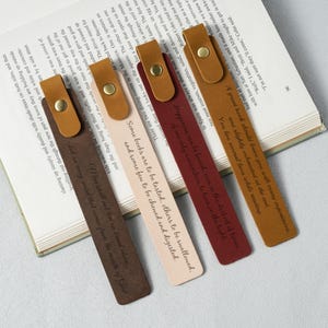 Puede incluir: Cuatro marcadores de cuero en tonos marrón, beige y burdeos, cada uno con un cierre de botón a presión dorado y texto en relieve. Los marcadores están sobre un libro abierto, ideales para la lectura.