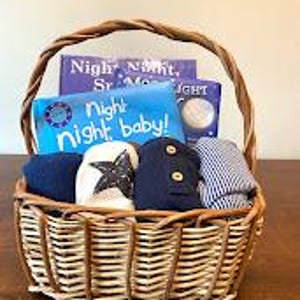 May include: A wicker basket containing baby essentials. It holds two children's books, navy socks with a star design, and two rolled-up outfits. The books are titled "Night Night, Sr. Moon" and "Night Night baby!"