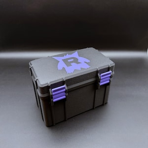 Könnte beinhalten: Schwarze Aufbewahrungsbox mit lila Akzenten. Die Box hat eine lila Grafik auf dem Deckel und lila Verschlüsse. Die rechteckige Box scheint aus einem strapazierfähigen Material zu bestehen.