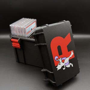 May include: Black storage case with a red latch and a red "R" logo with a cartoon character on the front. The case is open, revealing several clear plastic card holders.