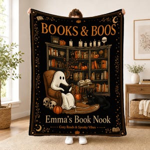 May include: A black throw blanket featuring the text BOOKS & BOOS, Emma's Book Nook, and Cozy Reads & Spooky Vibes. The design shows a ghost reading in an armchair, a black cat, a bookshelf, pumpkins, skulls, and candles in orange and white.