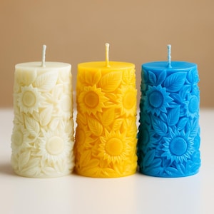 Peut inclure: Trois bougies piliers, ivoire, jaune et bleu, chacune sculpt&eacute;e avec un motif de tournesol et de feuilles. Les bougies ont une forme cylindrique et une m&egrave;che sur le dessus. Les bougies sont non parfum&eacute;es et conviennent &agrave; la d&eacute;coration int&eacute;rieure.