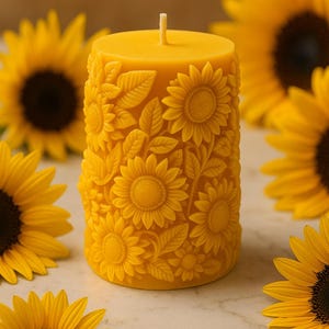 Peut inclure: Une bougie pilier jaune avec un motif de tournesol. La bougie est finement sculpt&eacute;e avec des tournesols et des feuilles. La bougie est entour&eacute;e de tournesols aux p&eacute;tales jaunes et aux centres brun fonc&eacute;. La bougie est sur une surface en marbre blanc.
