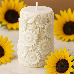 Peut inclure: Une bougie pilier blanche orn&eacute;e d'un motif de tournesol. La bougie est entour&eacute;e de tournesols jaunes avec des centres brun fonc&eacute;. La bougie a une m&egrave;che et est d&eacute;cor&eacute;e de sculptures d&eacute;taill&eacute;es de tournesols et de feuilles.