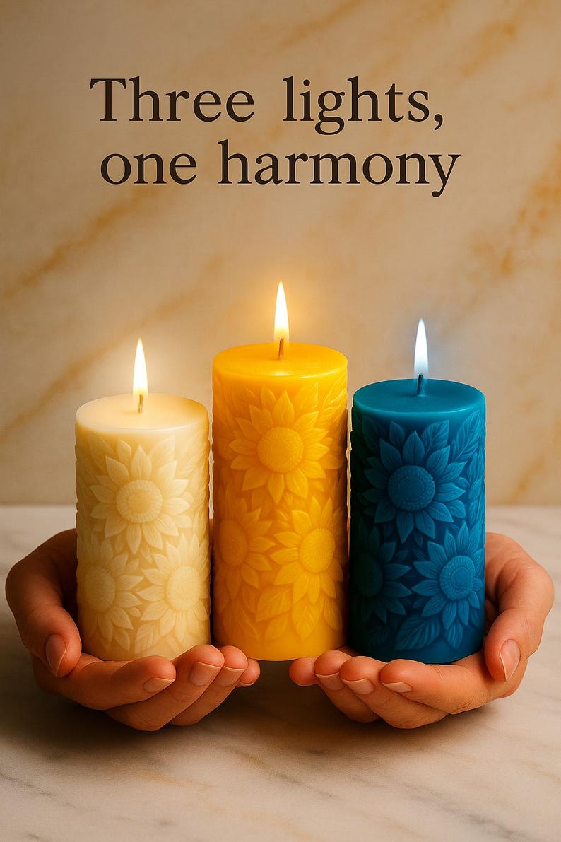 Peut inclure: Trois bougies allum&eacute;es en cr&egrave;me, jaune et bleu sarcelle, chacune avec un motif de tournesol. Les bougies sont tenues dans des mains en coupe. Le texte au-dessus indique : "Trois lumi&egrave;res, une harmonie."