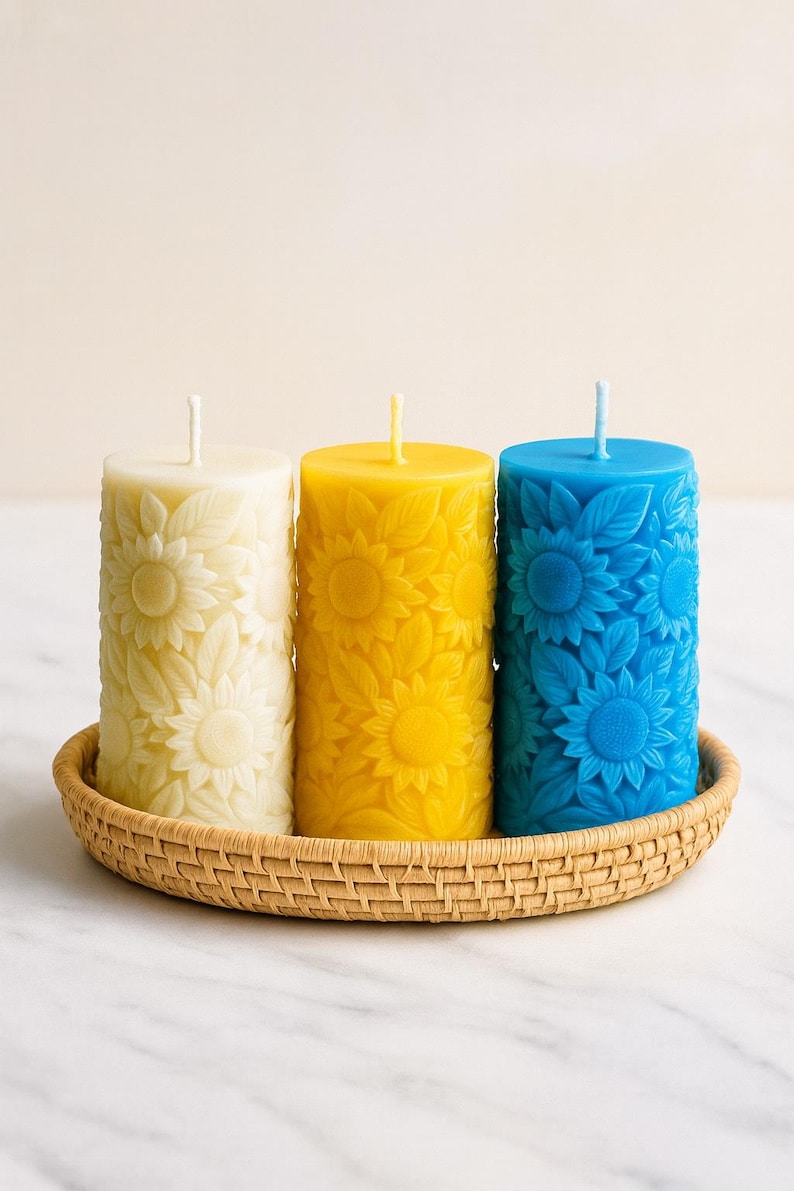 Peut inclure: Trois bougies cylindriques dans un panier tress&eacute;. Les bougies sont cr&egrave;me, jaune et bleu, chacune avec un motif de tournesol. Les bougies ont une m&egrave;che en haut. Le panier est rond et en mat&eacute;riau brun clair. Les bougies mesurent environ 10 cm de haut.