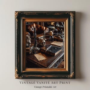 May include: Framed vintage art print featuring a dark, gothic still life. The image shows a desk with a skull, books, candles, and a quill. The frame is black with gold accents. Text at the bottom reads "VINTAGE VANITÉ ART PRINT" and "Vintage Printable Art."
