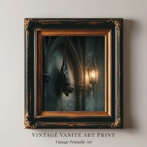 May include: Framed art print featuring a gothic scene with a bat hanging from an archway and a lit lantern. The print has a dark, moody color palette with the text "VINTAGE VANITÉ ART PRINT" and "Vintage Printable Art" at the bottom.