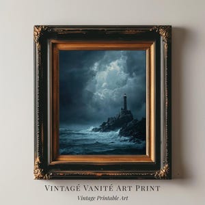May include: A framed art print depicting a lighthouse on a rocky coast under a stormy sky. The artwork is in a dark color palette with shades of blue and gray. The frame is ornate with a gold inner border and a black outer frame. Text at the bottom reads "VINTAGE VANITÉ ART PRINT" and "Vintage Printable Art."