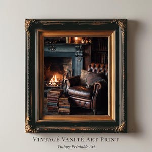 May include: A framed art print featuring a cozy interior scene. The print showcases a leather armchair, a fireplace with a burning fire, and stacks of books. The frame is black with gold accents. Text at the bottom reads "VINTAGE VANITÉ ART PRINT" and "Vintage Printable Art."