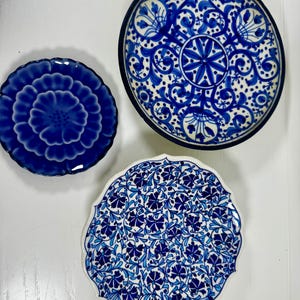 Puede incluir: Tres platos decorativos de cerámica con diseños florales azules y blancos. Los platos varían en tamaño y patrón, uno con un diseño de flor grande, otro con un patrón circular detallado y el tercero con un motivo floral repetitivo.