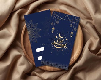 May include: Two navy blue Eid Mubarak greeting cards with gold accents, featuring a floral design and hanging lanterns. The cards are displayed on a wooden tray, set against a backdrop of draped fabric.