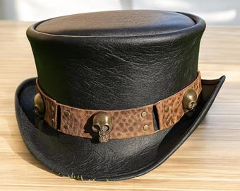 May include: A black top hat with a brown leather band featuring skull accents. The hat has a classic design with a rounded crown and a wide brim. The band is adorned with metal rivets.