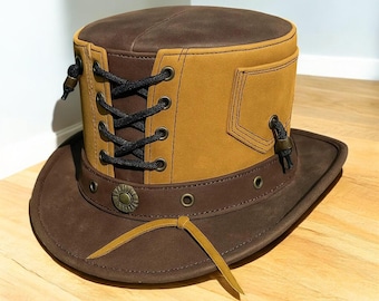 May include: A brown and tan leather top hat with a wide brim. The hat features a laced front, a decorative metal button, and a small pocket. The hat is designed with a steampunk aesthetic.