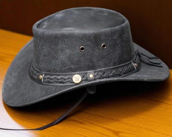 Puede incluir: Sombrero de vaquero gris oscuro con una banda de cuero trenzado y remaches decorativos. El sombrero tiene un ala ancha y una corona estructurada con dos ojales. Se adjunta una correa de barbilla de cuero.