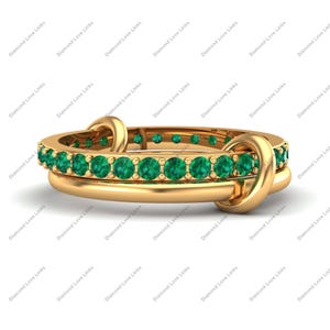 May include: Two gold rings stacked together. The top ring features a row of small, round, bright green gemstones. The rings are connected by a gold loop design. The rings are on a white background.