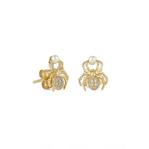 May include: A pair of gold-colored spider stud earrings. Each earring features a spider design with a pearl at the top and a cluster of small, clear stones on the body. The earrings are set against a white background.