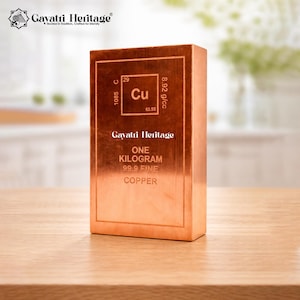 May include: A copper bar with the text "ONE KILOGRAM 99.9 FINE COPPER" and the chemical symbol "Cu". The bar is rectangular and has a polished finish. The bar is sitting on a wooden surface.