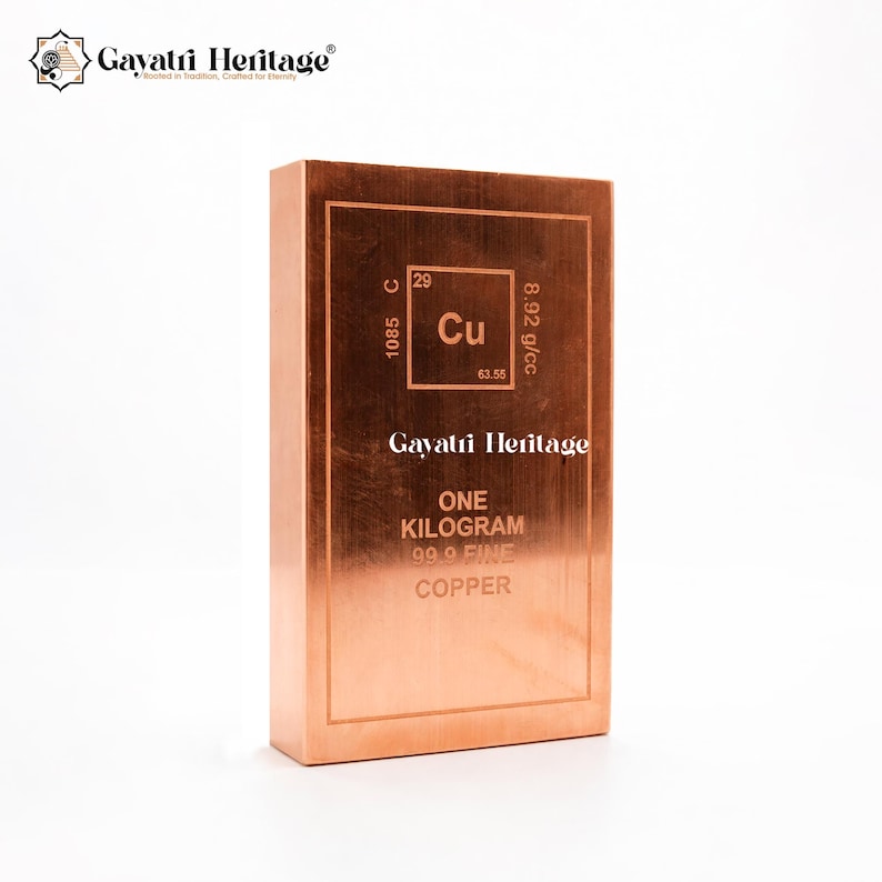 May include: A copper bar with the text "ONE KILOGRAM 99.9 FINE COPPER" and the Gayatri Heritage logo. The bar features the element symbol Cu, atomic number 29, and other scientific data. The bar is a reddish-brown color.