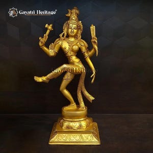 Puede incluir: Una estatua dorada de latón de una deidad danzante, con múltiples brazos y detalles ornamentados. La estatua está sobre una base cuadrada con intrincadas tallas. La deidad está adornada con joyas y sostiene objetos en sus manos. La estatua mide unos 46 cm de altura.